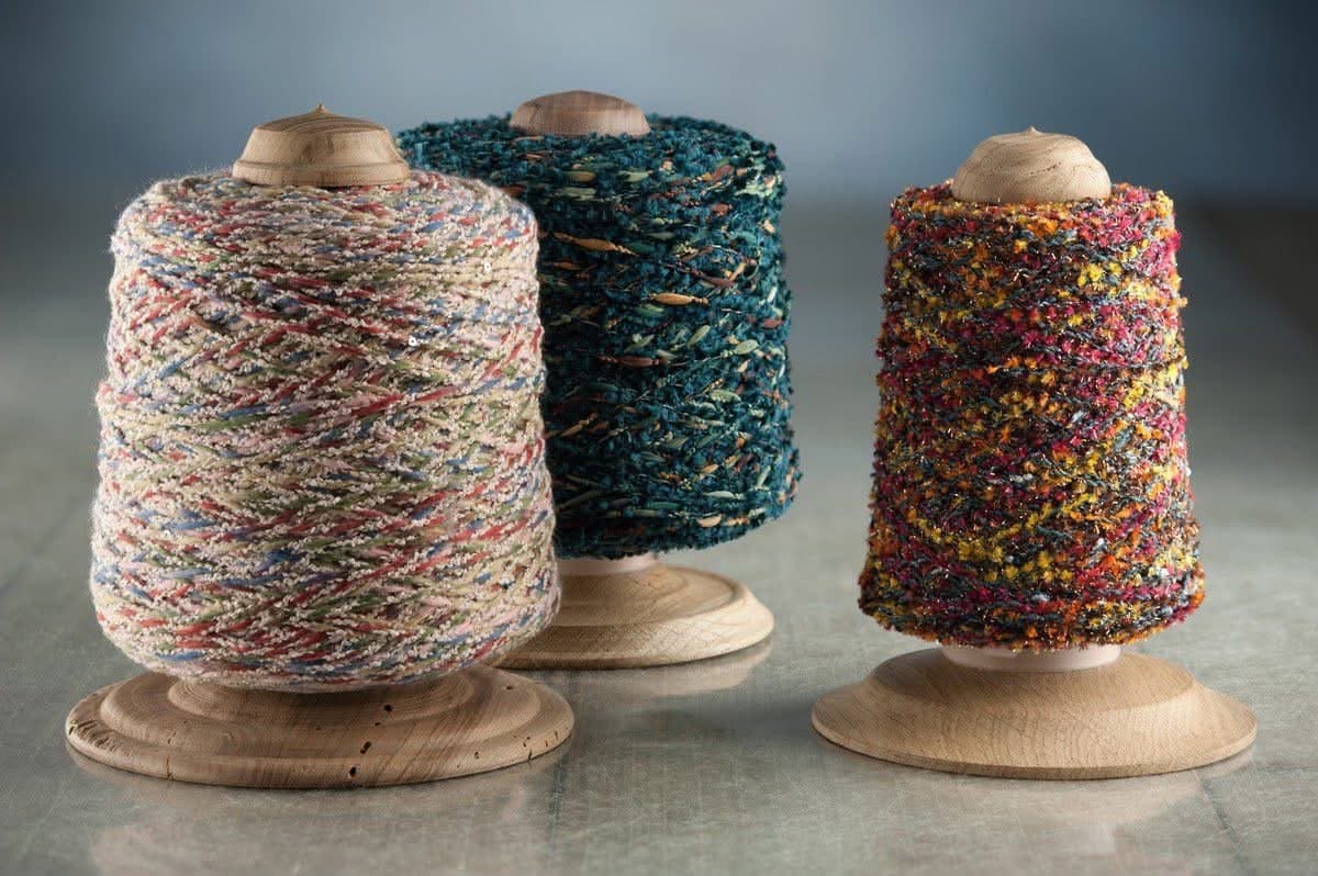 Three spools of textured, variegated yarn in teal, pink, and orange on wooden stands.
