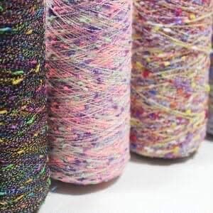 Close-up of multiple spools of textured, multi-colored yarn featuring vibrant, speckled flecks throughout.