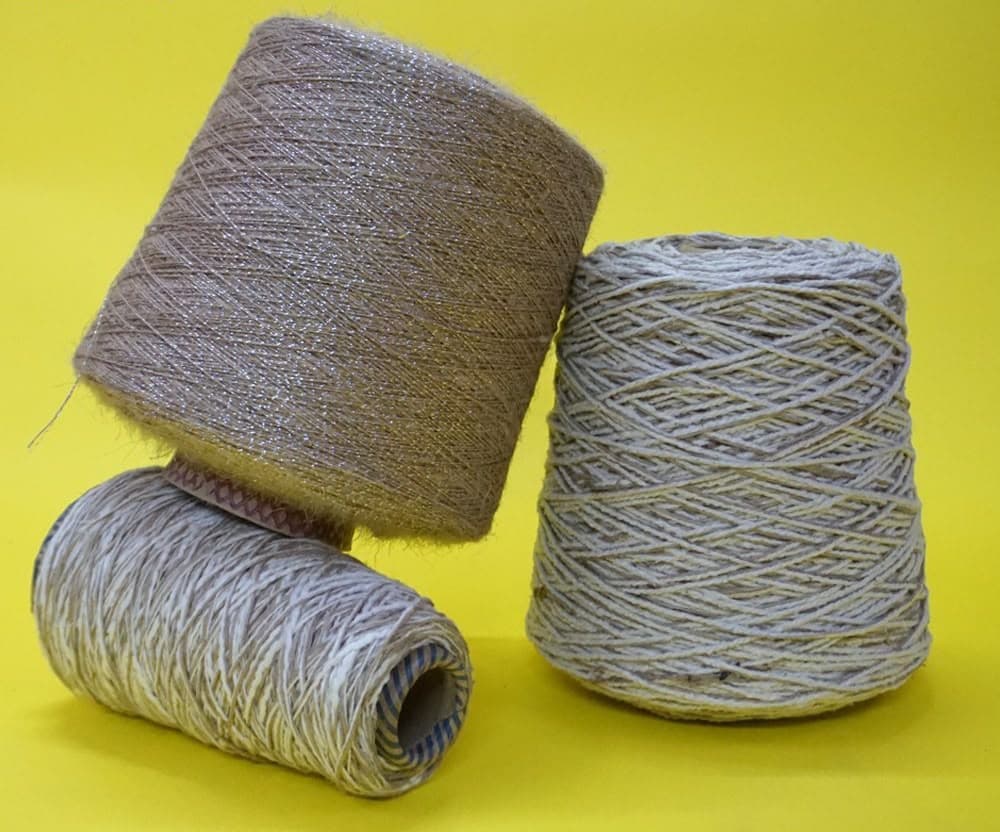 Three spools of shimmering brown and variegated beige yarn against a bright yellow background.