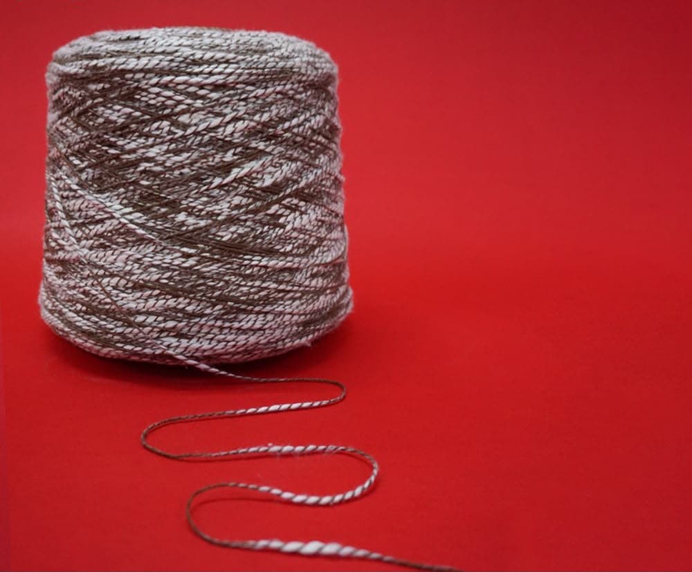 Variegated brown and white yarn cone on a vibrant red background with a winding strand.